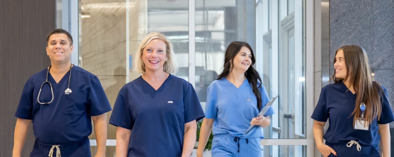 4 healthcare workers smiling and walking towards the camera