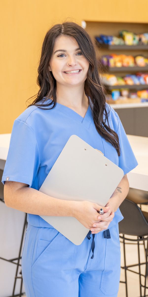 Woman in scrubs smiling and holding a clipboard