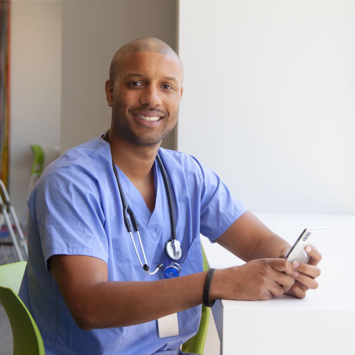 Male Healthcare Worker with a phone in their hands and smiling at the camera