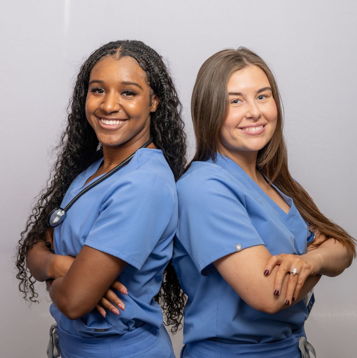 Two female healthcare workers standing back to back and smiling at the camera