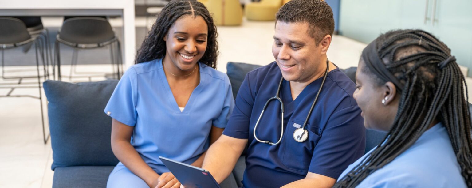 2 women and a man in scrubs smiling looking at tablet