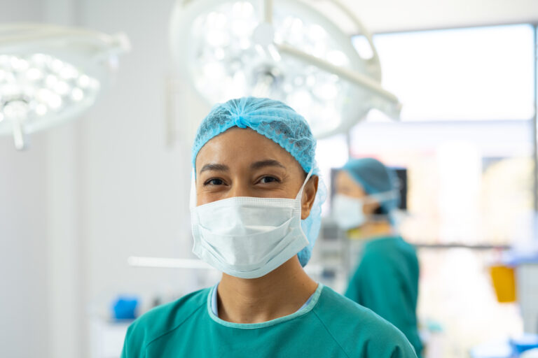 Portrait of smiling biracial female surgeon in mask and cap in operating theatre copy space Hospital medical and healthcare services - Staffdna